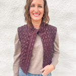 A woman wearing a deep burgundy quilted vest with zipper front over a lightweight wool blend sweater in a mocha color and denim jeans from Daze