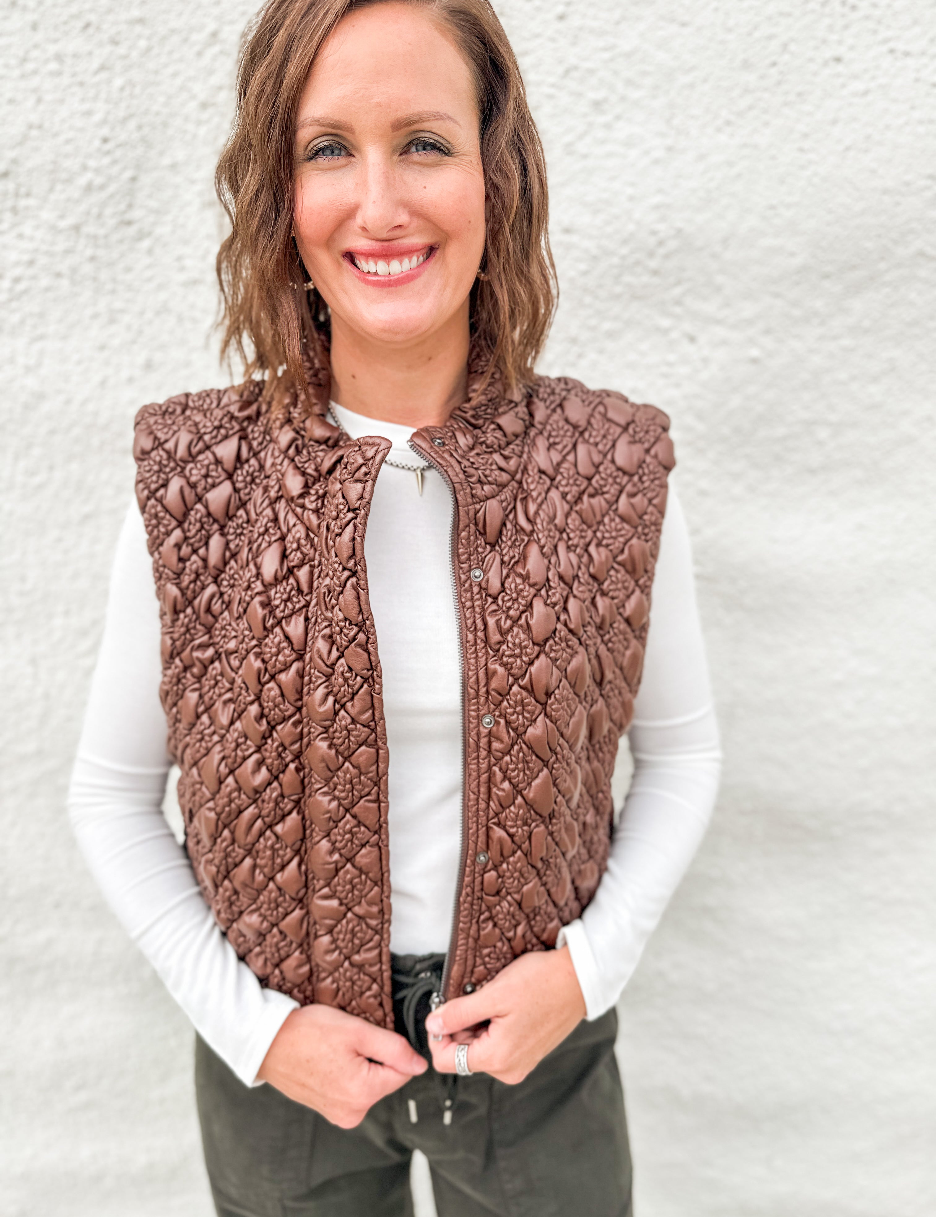 Model wearing a quilted brown vest with a faux leather look layered over a white ribbed long sleeve tee and green barrel denim from Daze