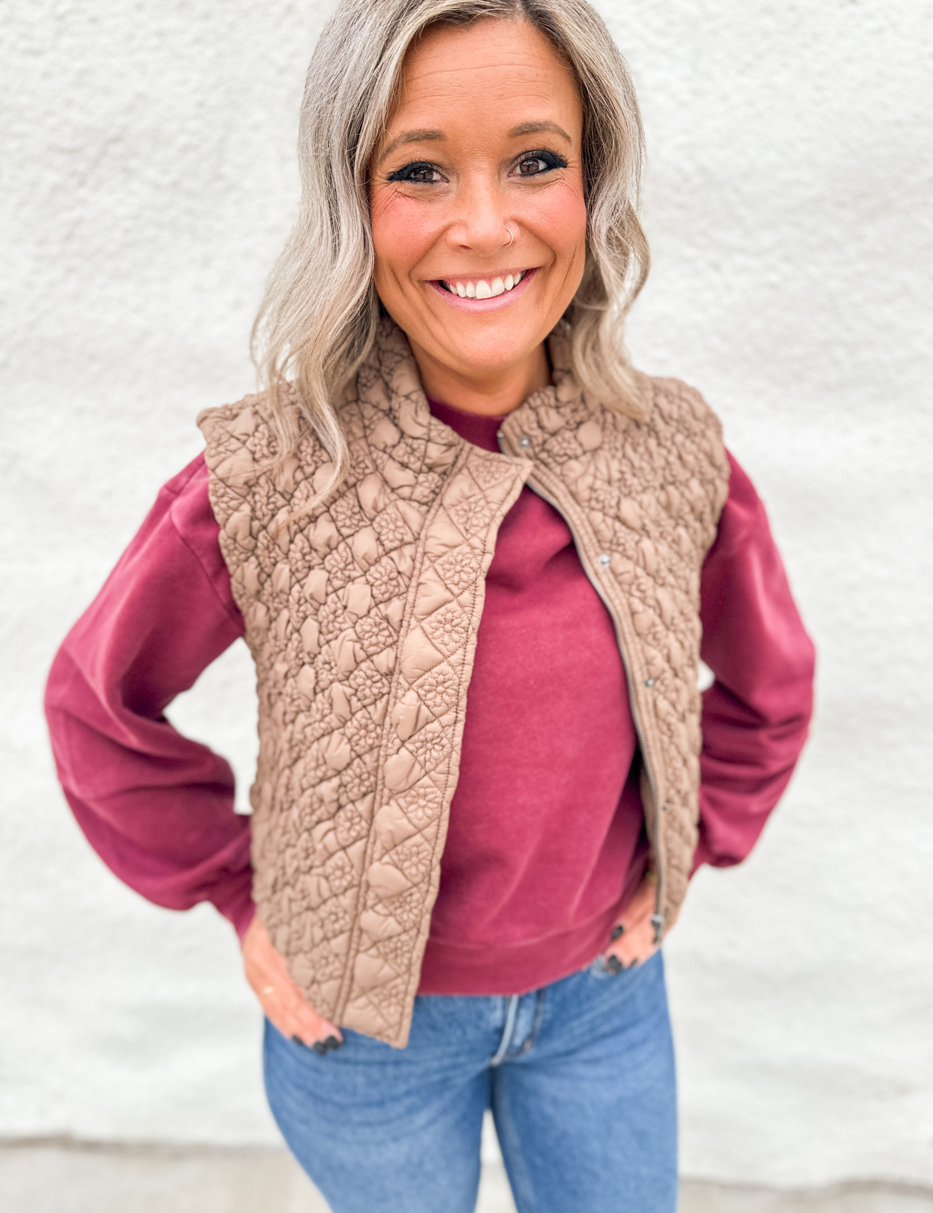 Woman wearing a light brown quilted vest with zipper front over a washed cherry color crewneck sweatshirt from Thread & Supply