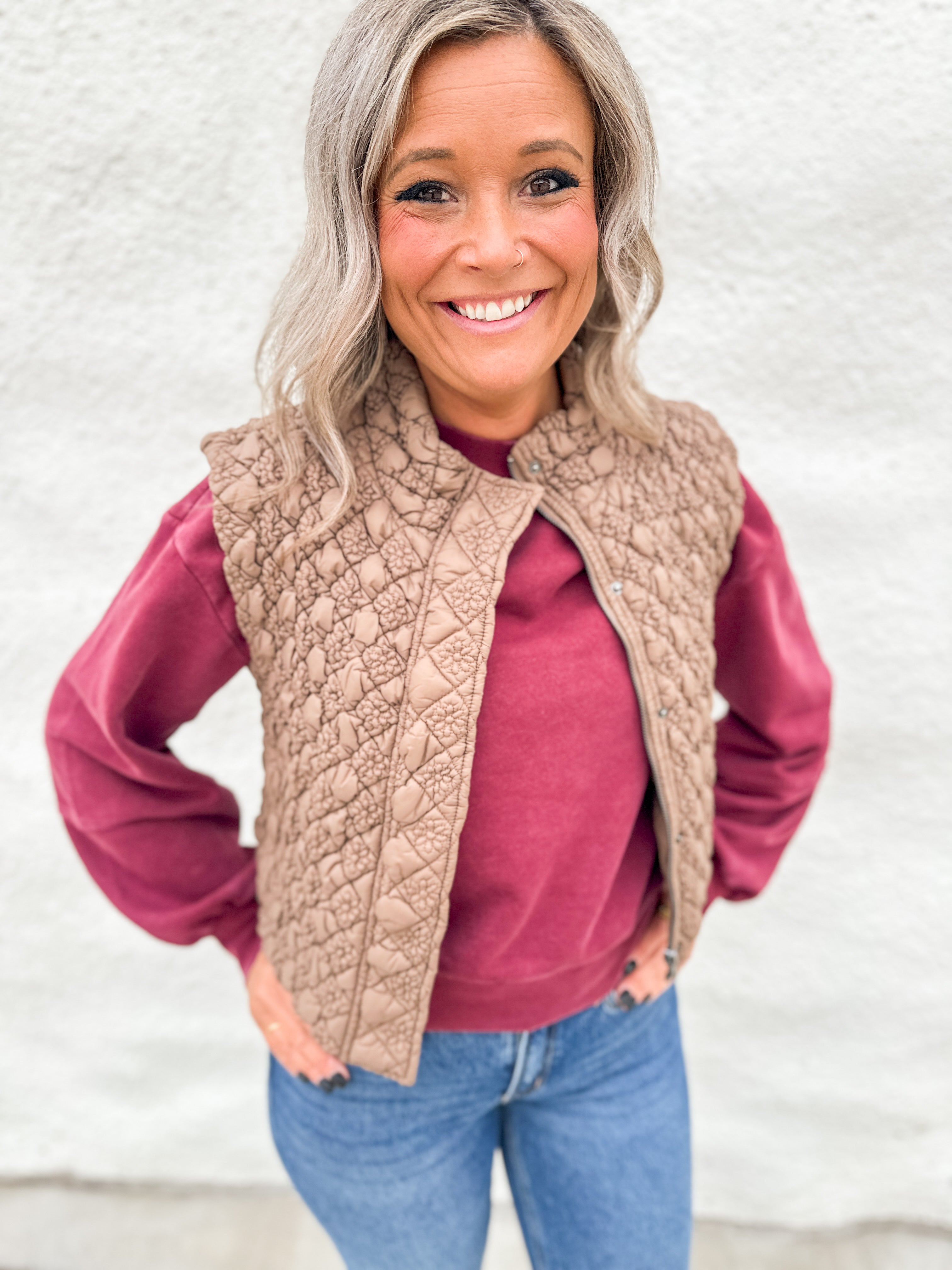 Woman wearing a light brown quilted vest with zipper front over a washed cherry color crewneck sweatshirt from Thread & Supply