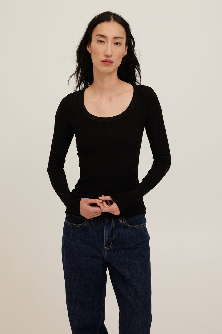 Person wearing a black ribbed long-sleeve top and dark jeans against a plain background