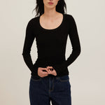 Person wearing a black ribbed long-sleeve top and dark jeans against a plain background