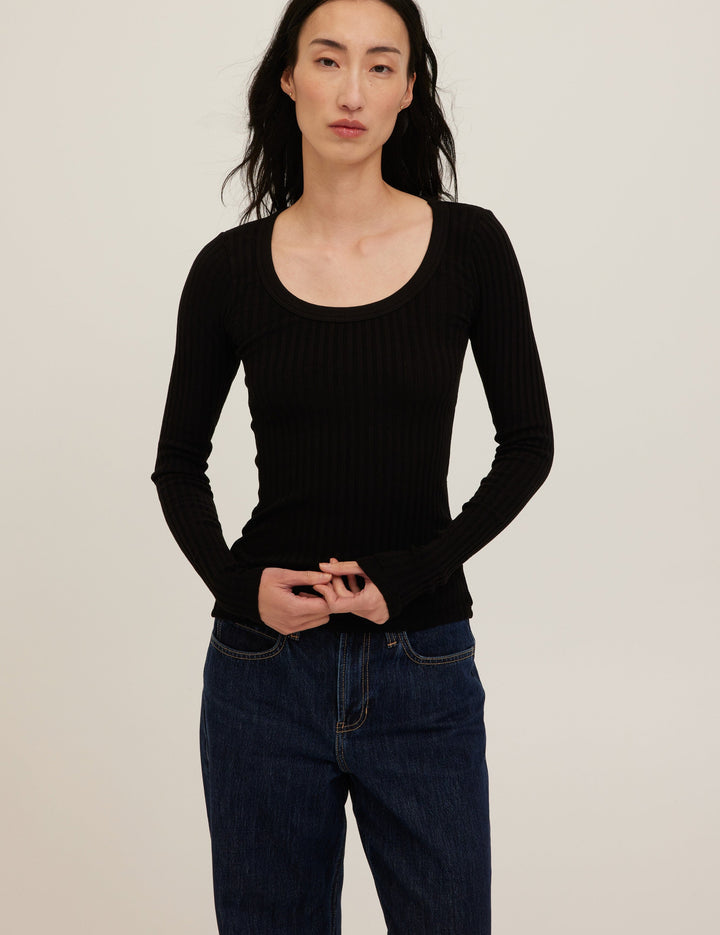 Person wearing a black ribbed long-sleeve top and dark jeans against a plain background