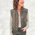 Woman wearing a quilted green vest with a faux leather look and zipper front layered over a distressed long sleeve v neck tee and green tie waist barrel jeans from Daze