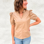 Woman wearing light brown faux leather short sleeve top with v neck collar and ruched shoulder sleeve detail and Far Out denim from daze