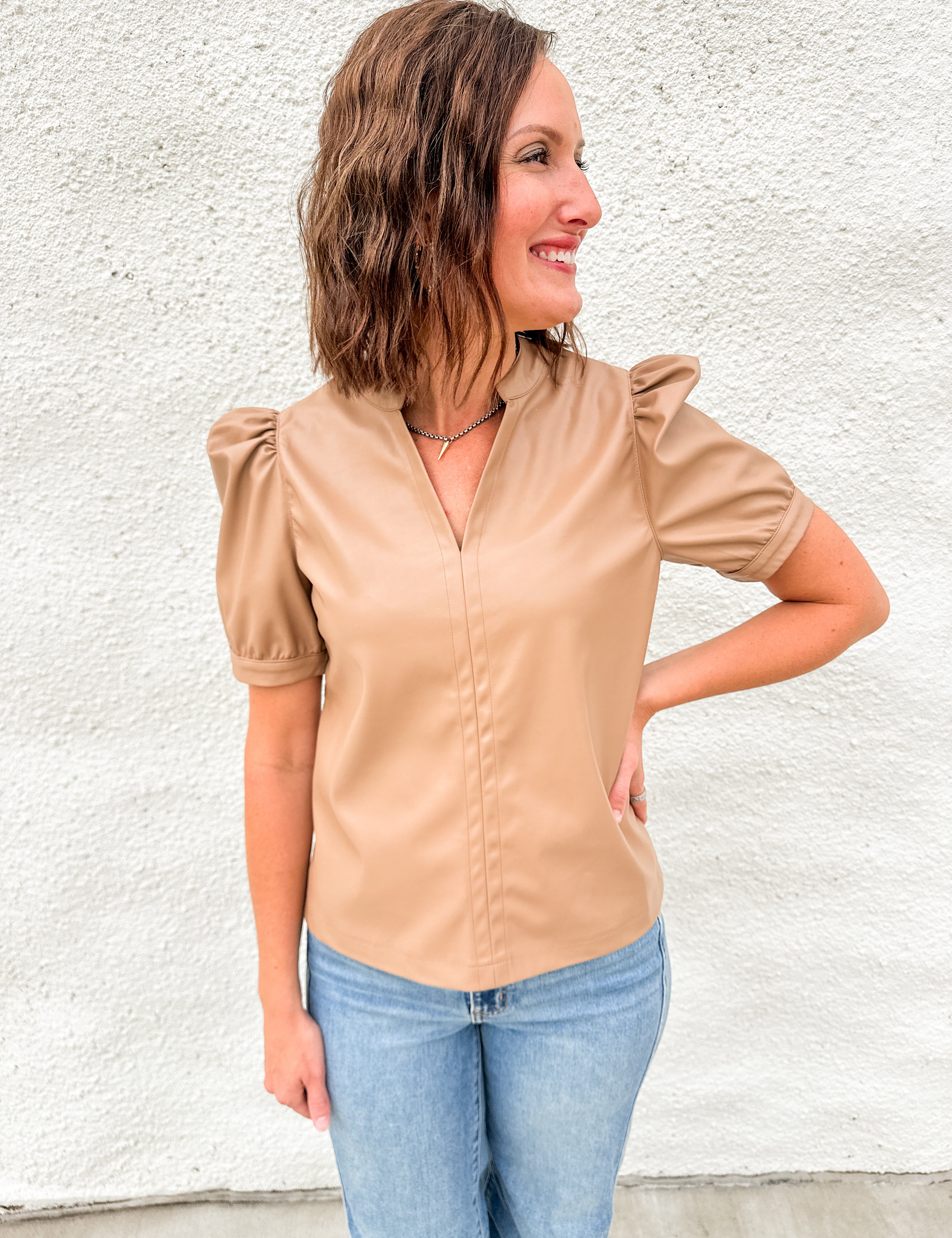 Woman wearing light brown faux leather short sleeve top with v neck collar and ruched shoulder sleeve detail and Far Out denim from daze