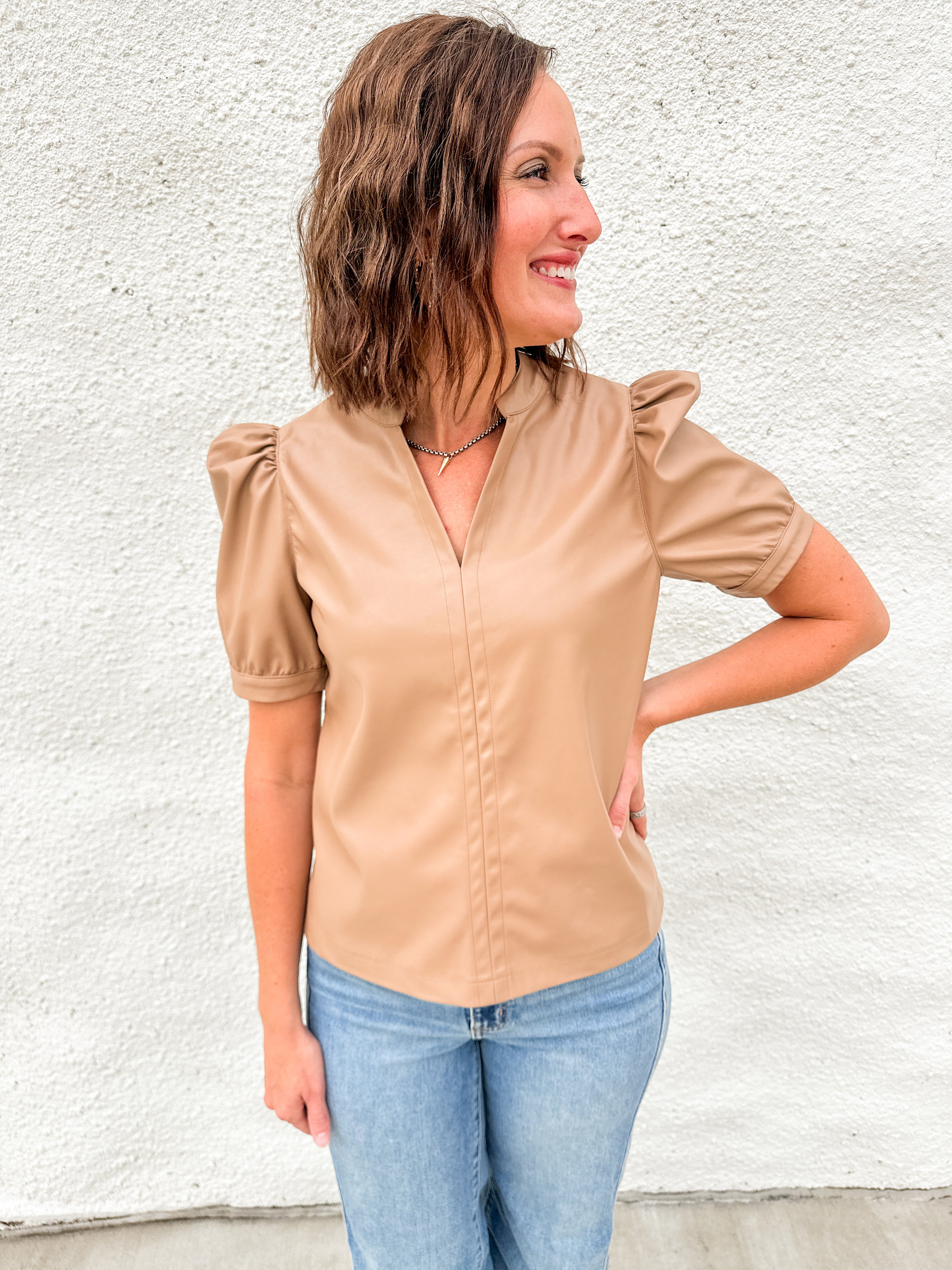 Woman wearing light brown faux leather short sleeve top with v neck collar and ruched shoulder sleeve detail and Far Out denim from daze