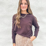 A woman modeling a dark chocolate colored knit sweater and a beige fawn print denim mini skirt against a textured white wall.