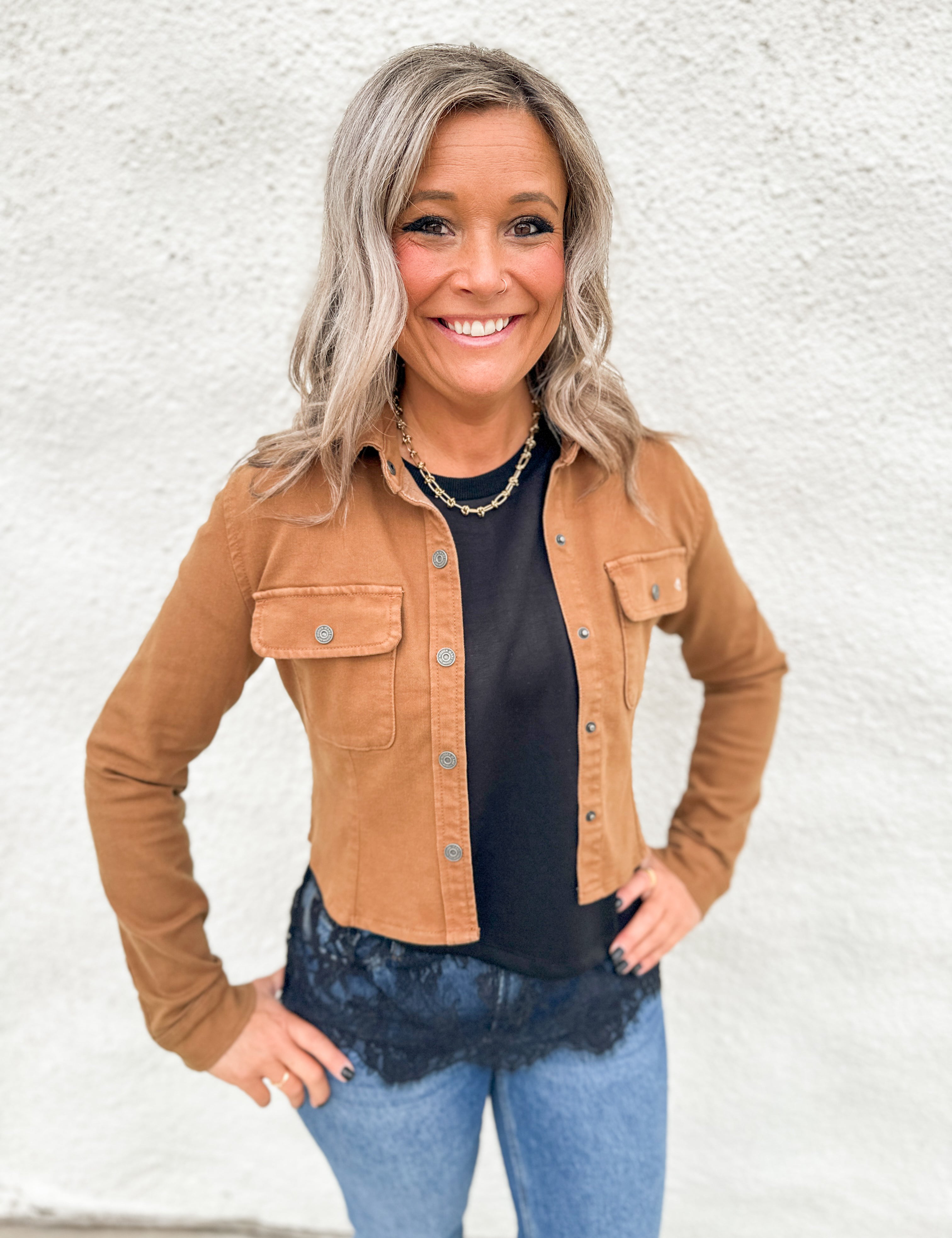 Model wearing a camel colored stretchy cropped denim jacket over a scuba black tee with asymmetrical lace hem detail and blue denim.