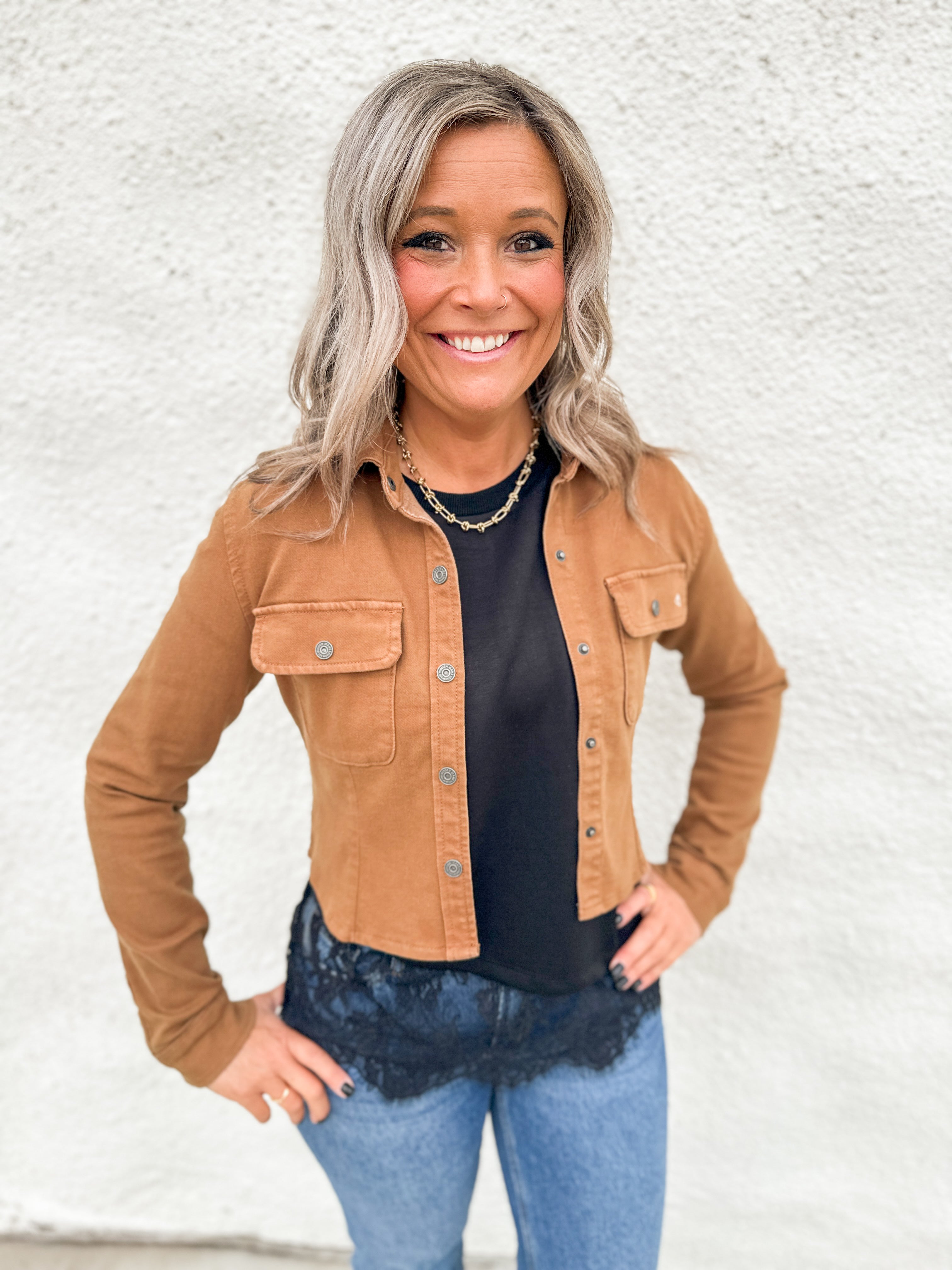 Model wearing a camel colored stretchy cropped denim jacket over a scuba black tee with asymmetrical lace hem detail and blue denim.