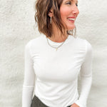 Woman wearing a soft lightly ribbed white long sleeved tee with green villa barrel jeans from Daze