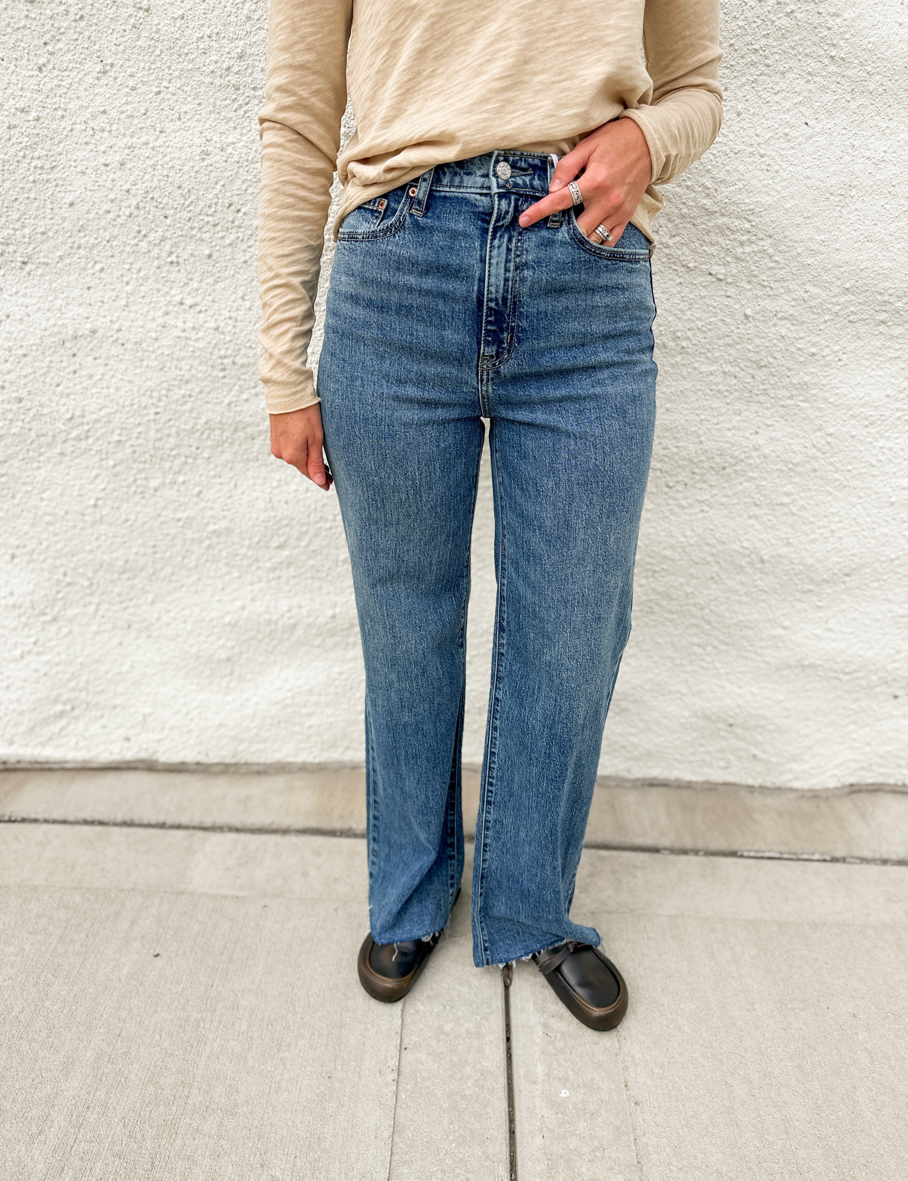 Woman wearing high rise wide leg denim with a raw hem, distressed black leather clogs and cream long sleeve top from Dear John