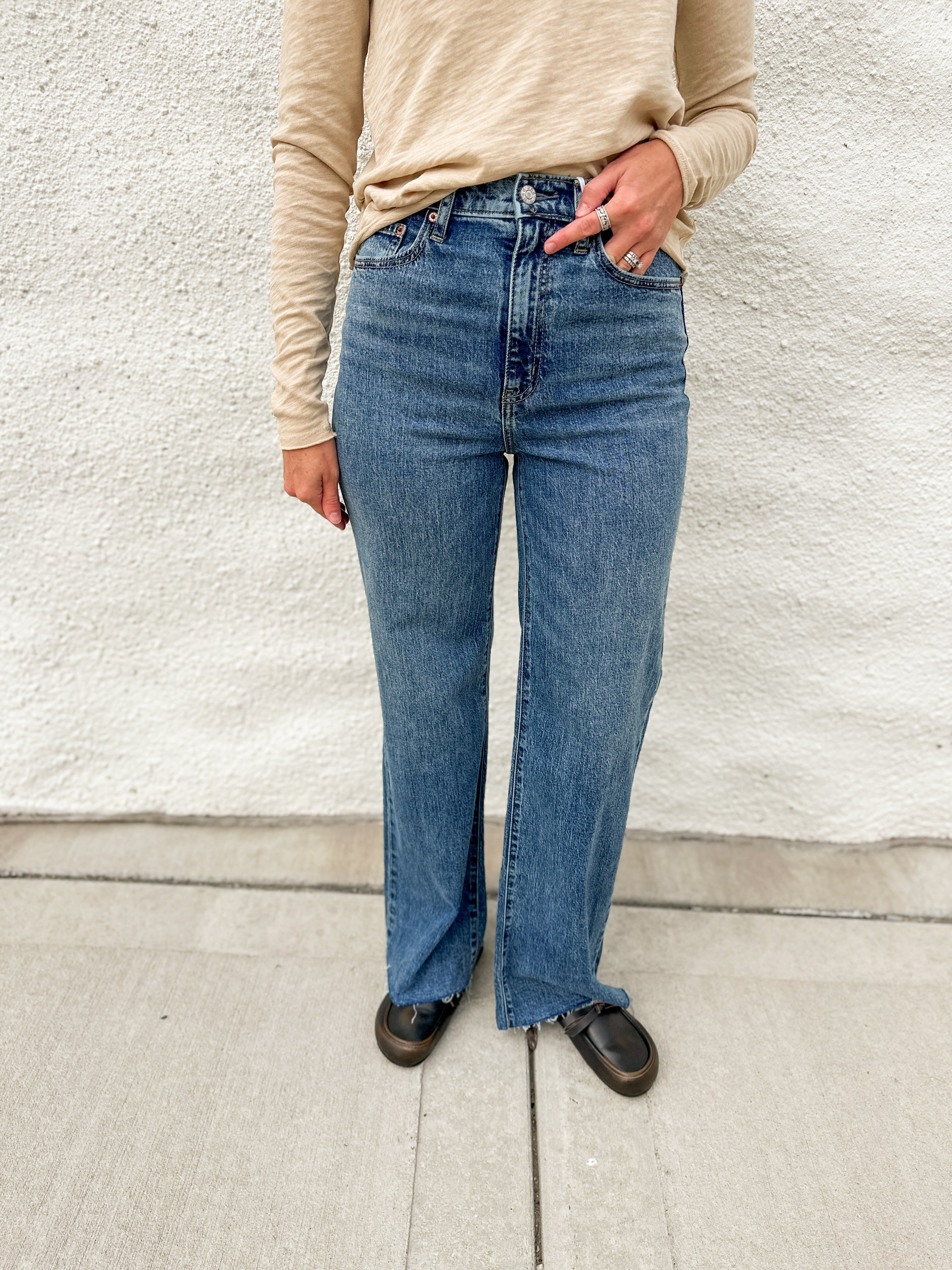 Woman wearing high rise wide leg denim with a raw hem, distressed black leather clogs and cream long sleeve top from Dear John