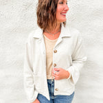 Woman wearing melange gray sweatshirt sweater with tailored collar and tortoise shell buttons in a terry fabrication with a distressed cream long sleeve top underneath and blue denim