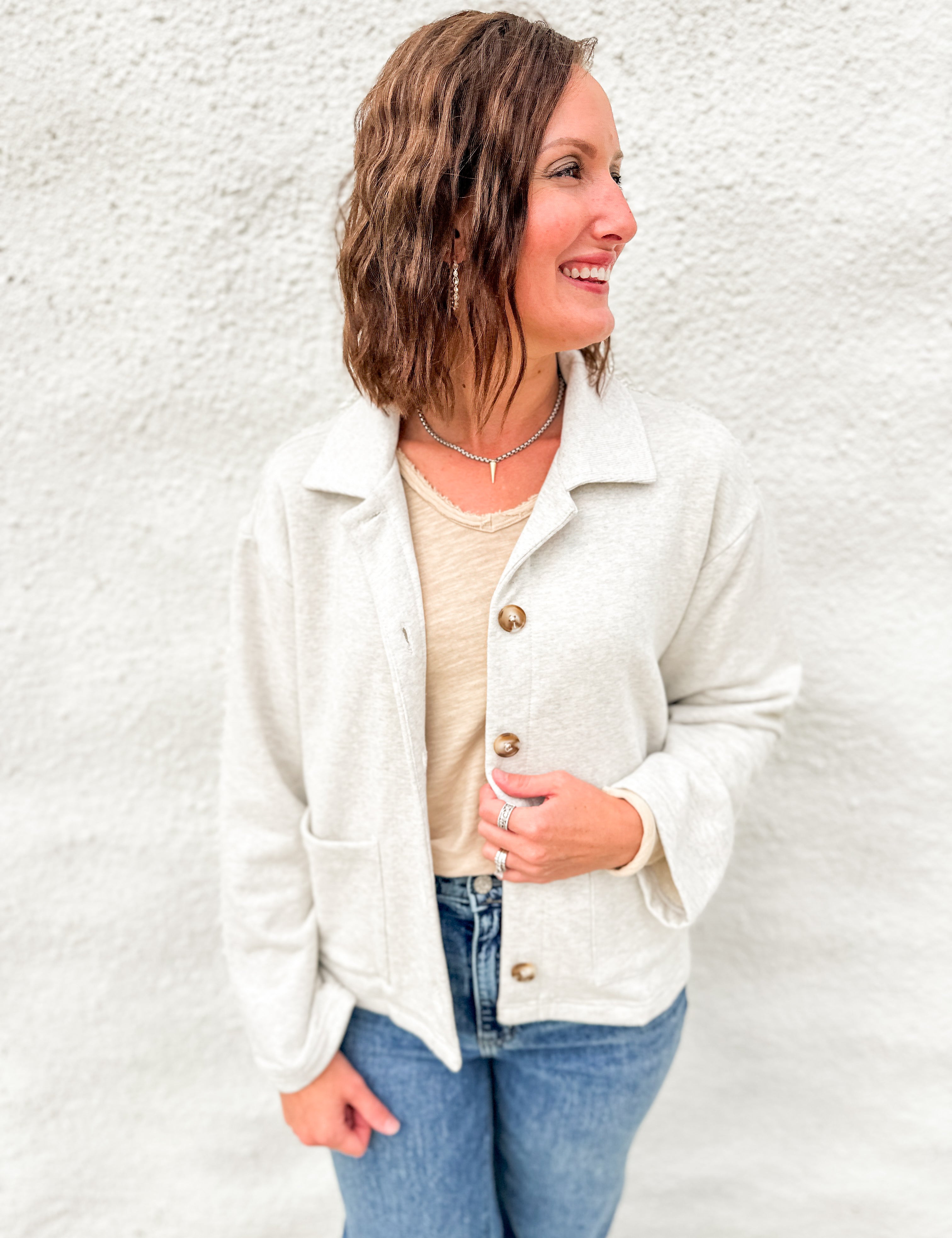 Woman wearing melange gray sweatshirt sweater with tailored collar and tortoise shell buttons in a terry fabrication with a distressed cream long sleeve top underneath and blue denim
