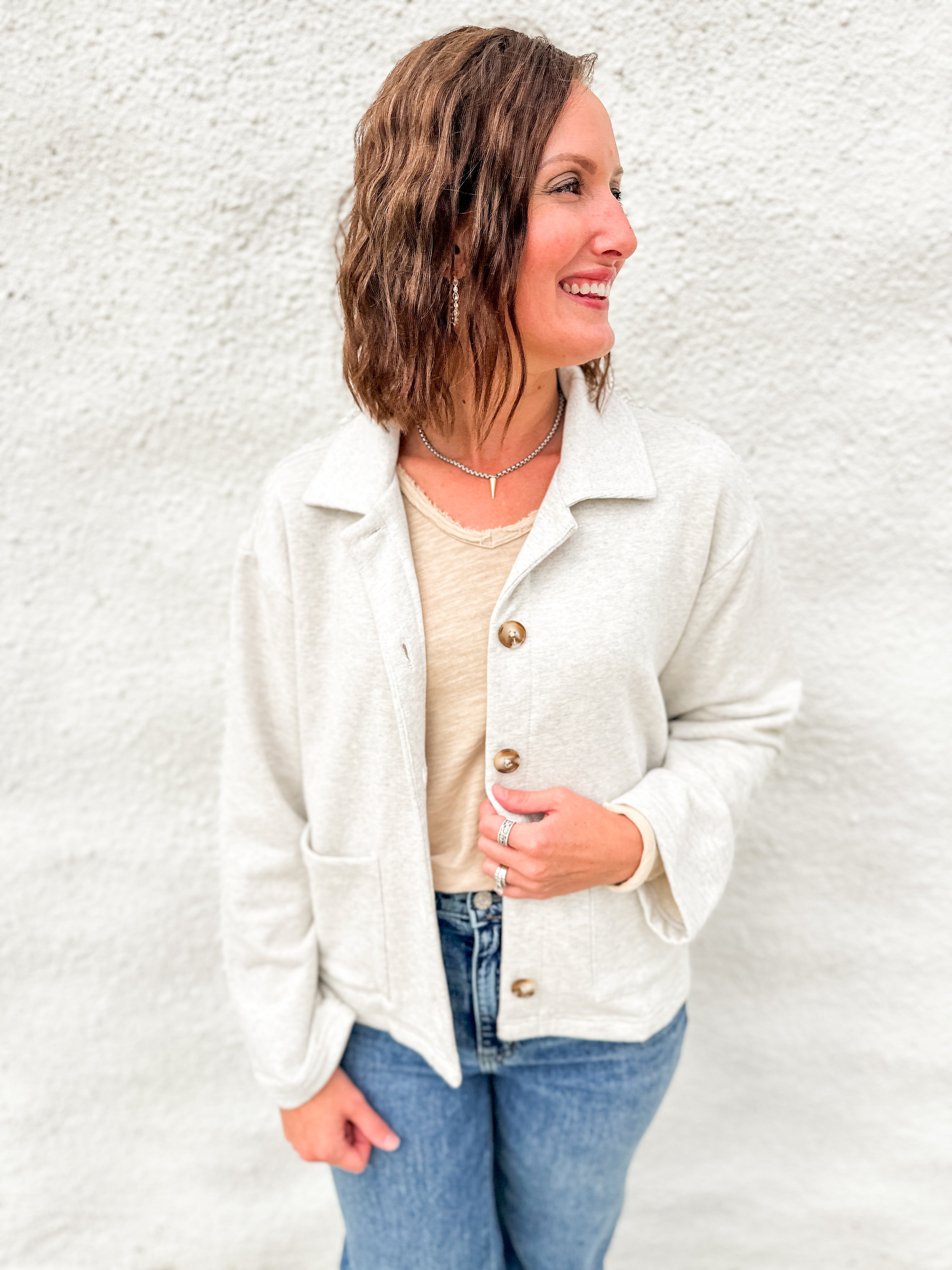 Woman wearing melange gray sweatshirt sweater with tailored collar and tortoise shell buttons in a terry fabrication with a distressed cream long sleeve top underneath and blue denim