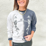 A girl wearing a black and white bleached sweatshirt with dancing skeletons and wearing faux leather pants with black sunglasses.