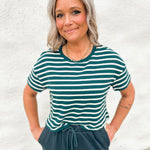 A woman wearing a textured green and white stripe tee with green drawstring pants against a white