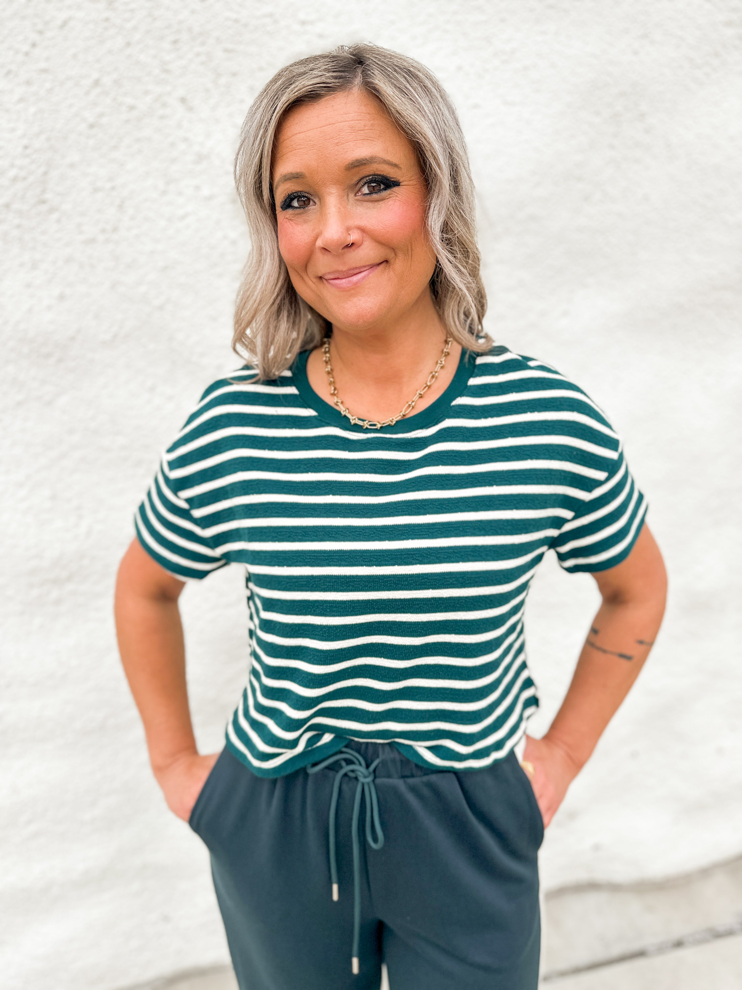 A woman wearing a textured green and white stripe tee with green drawstring pants against a white