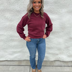 Model wearing a crewneck sweatshirt in a washed burgundy color with straight leg denim and faux snakeskin clogs with gold stud detail