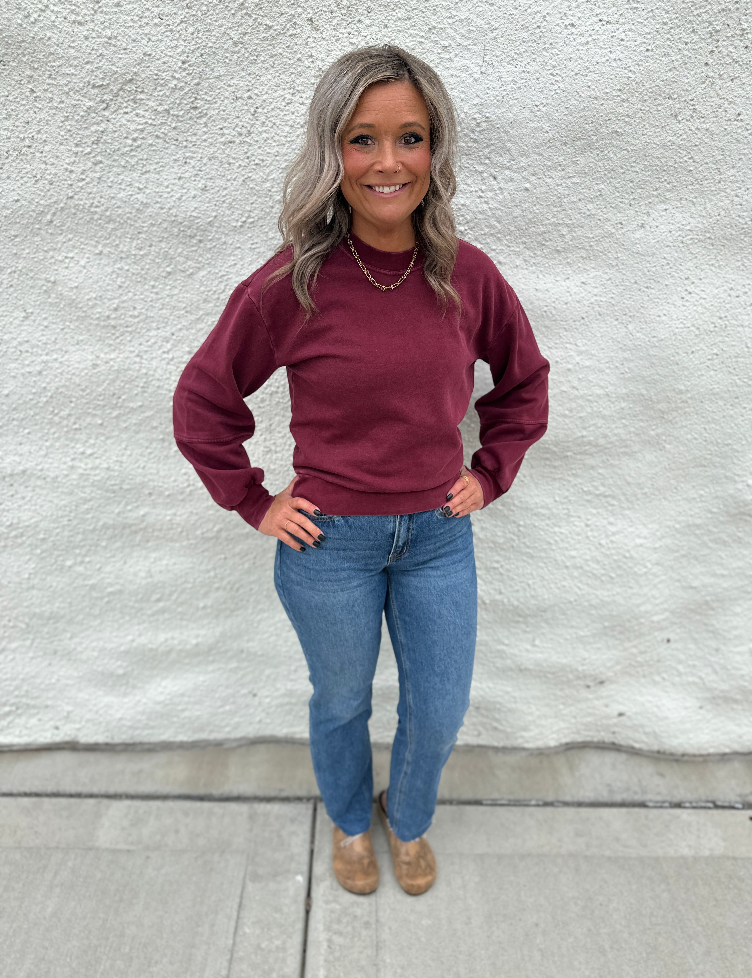 Model wearing a crewneck sweatshirt in a washed burgundy color with straight leg denim and faux snakeskin clogs with gold stud detail
