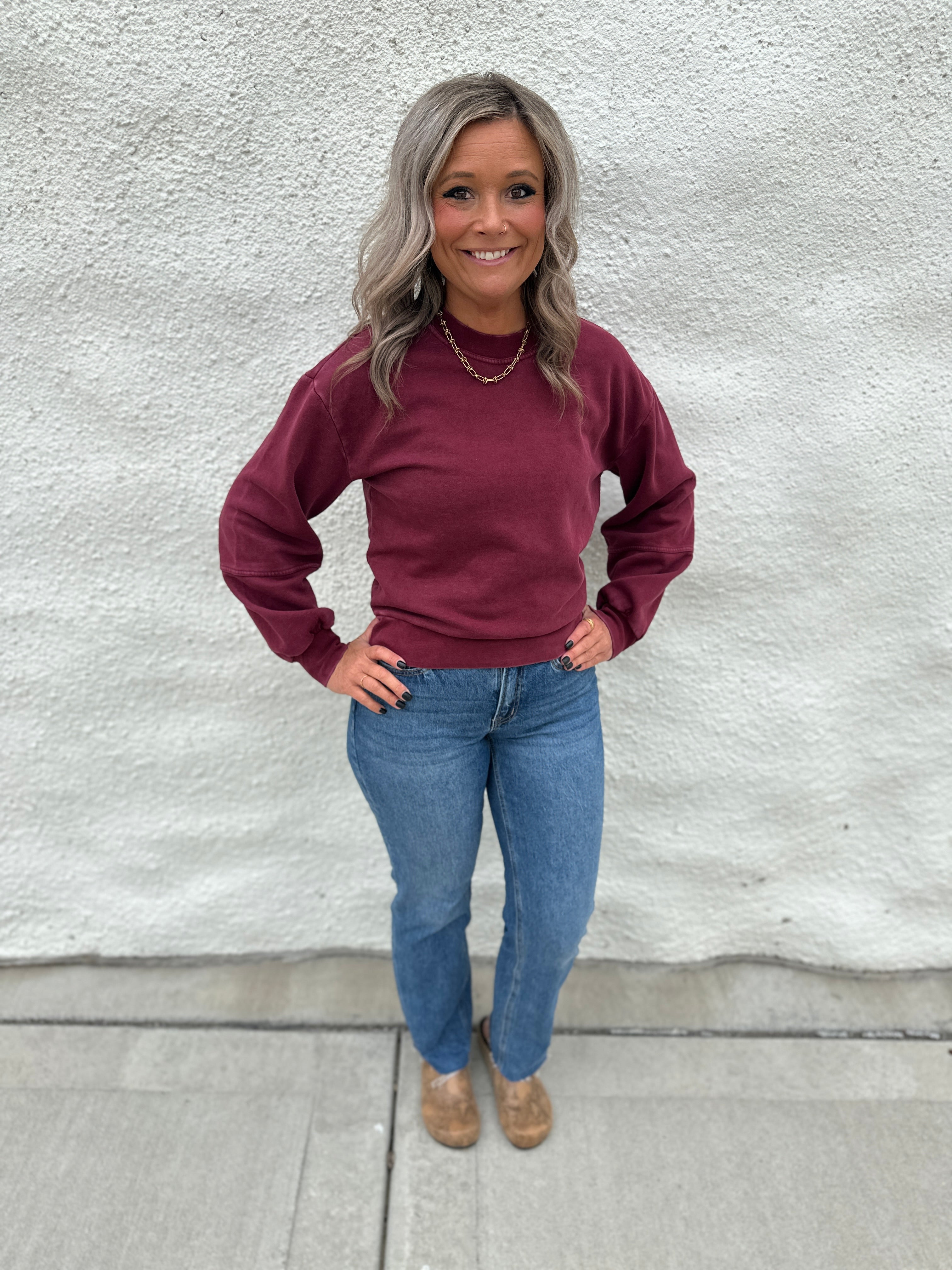 Model wearing a crewneck sweatshirt in a washed burgundy color with straight leg denim and faux snakeskin clogs with gold stud detail