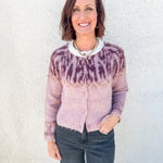 A smiling woman with short brown hair stands against a white textured wall wearing a fuzzy knit cardigan with a maroon and dusty pink Fair Isle yoke pattern, paired with dark gray jeans.