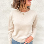 Model wearing a cream colored lightweight crewneck sweater with wool blend, stitched v detail at neckline