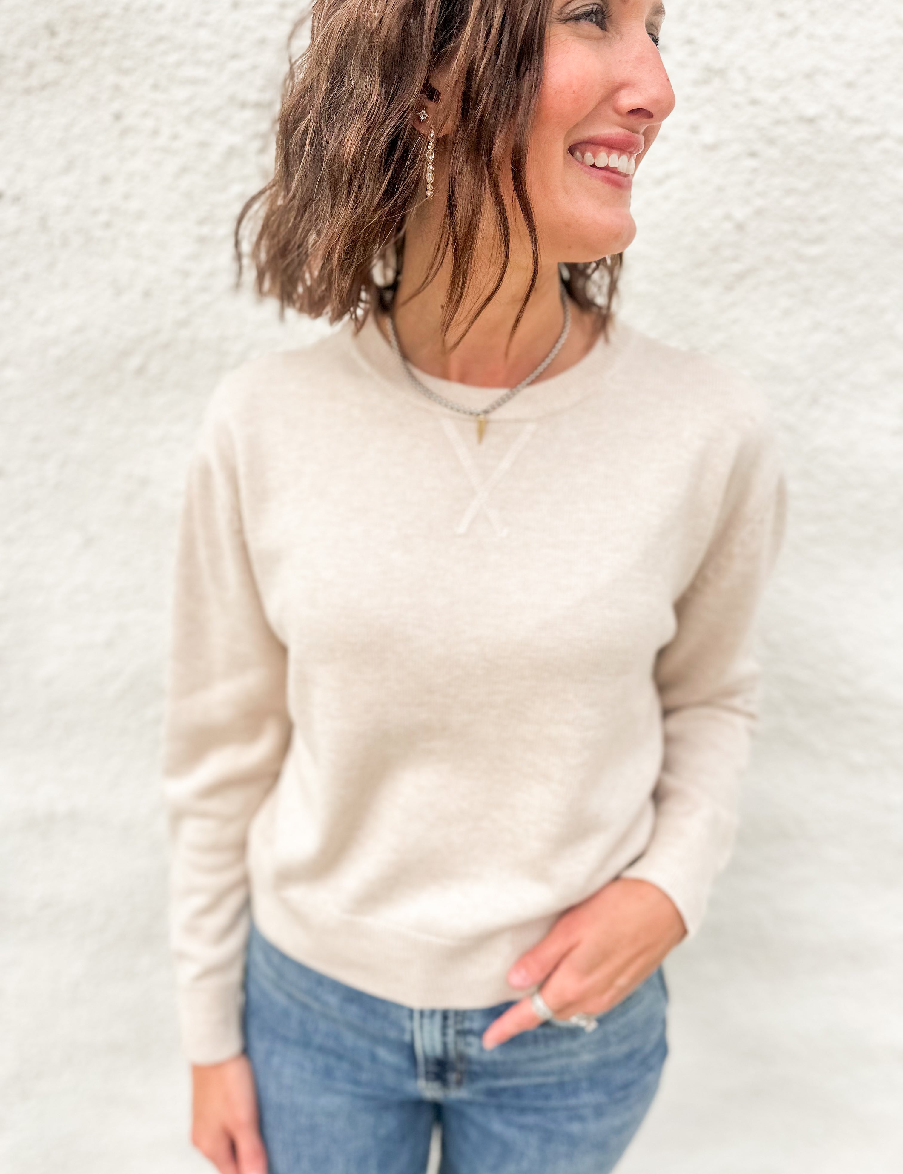 Model wearing a cream colored lightweight crewneck sweater with wool blend, stitched v detail at neckline
