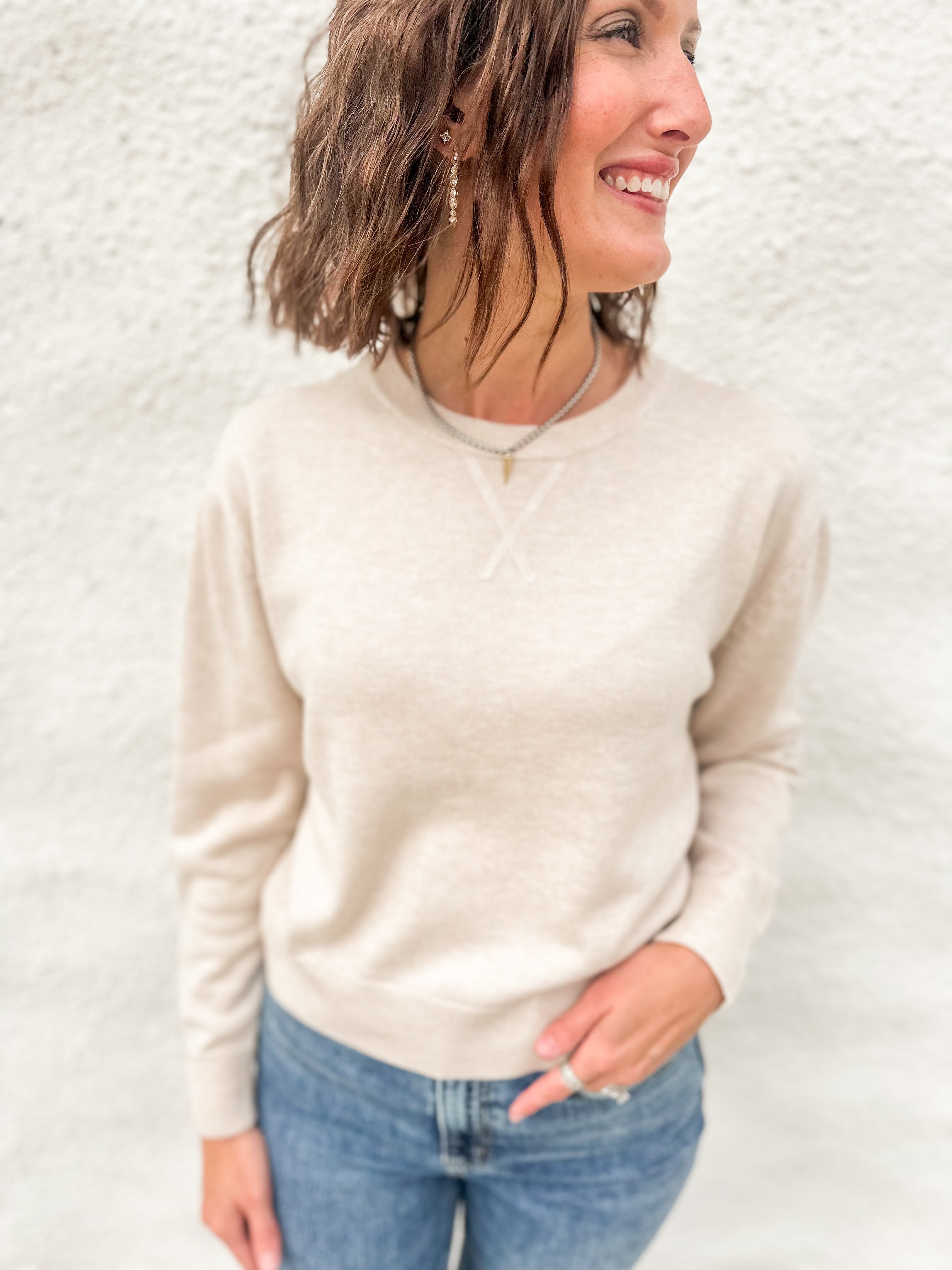 Model wearing a cream colored lightweight crewneck sweater with wool blend, stitched v detail at neckline