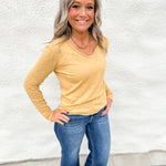 A woman wearing a long sleeve top with rolled hems wearing blue jeans standing in front of a white wall.