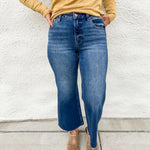 Model wearing a high rise wide leg denim in a dark wash with fading on the legs with a raw hem and gold colored distressed long sleeve tee shirt and faux snakeskin clogs with gold studs