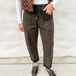 Dark green barrel denim with front pockets and drawstring waistband, long sleeve lightly ribbed long sleeve top and brown faux leather look vest with stitched details, zippered front and buttons, distressed black leather clogs