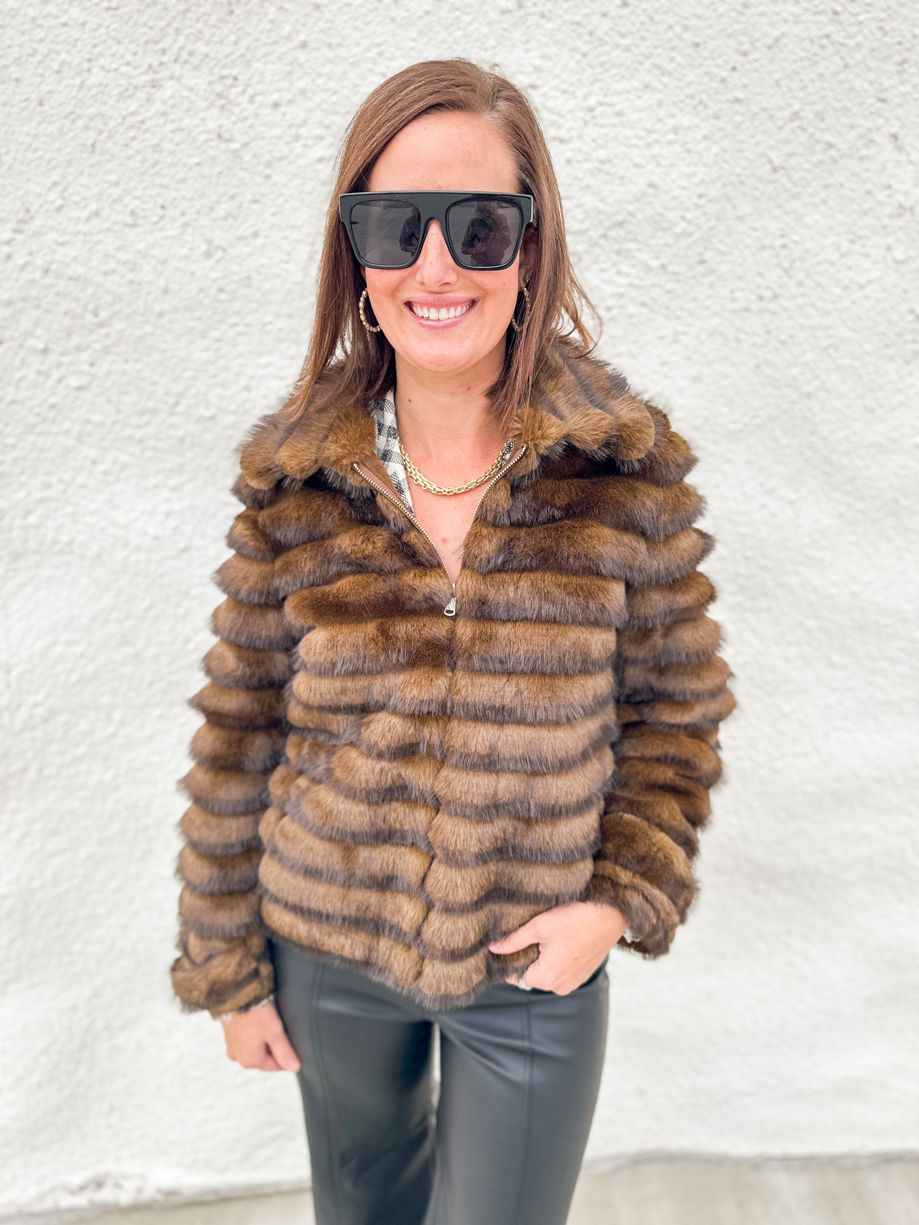 Faux fur jacket with silver zippered front, tiered textured layers of brown fur with dark brown tips, button cuff sleeve detail on model
