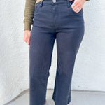 A person wearing black wide-leg jeans, an olive green long-sleeve top, and brown mesh flats in a Mary Jane shoe style, standing against a white textured wall.