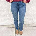 Woman wearing straight leg denim with a raw hem in a classic medium stonewash with a crewneck sweatshirt in a washed cranberry color and faux snakeskin clogs with gold studs