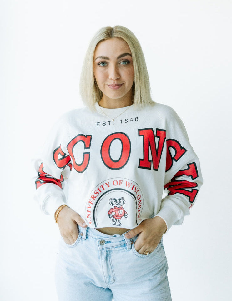 Person wearing a white sweatshirt with red text and a logo, standing against a white background