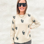A woman wearing a tan crewneck sweater with printed skulls and gray denim from Liverpool los angeles